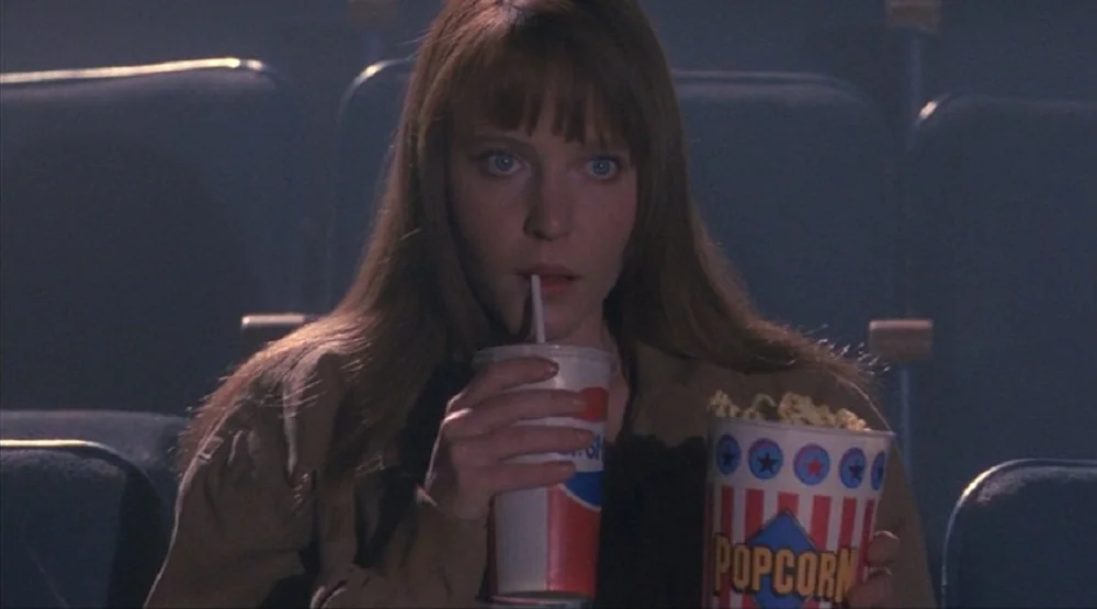 Lisa Wilcox as Alice Johnson. She's sipping from a cup of soda, with popcorn in her other hand.