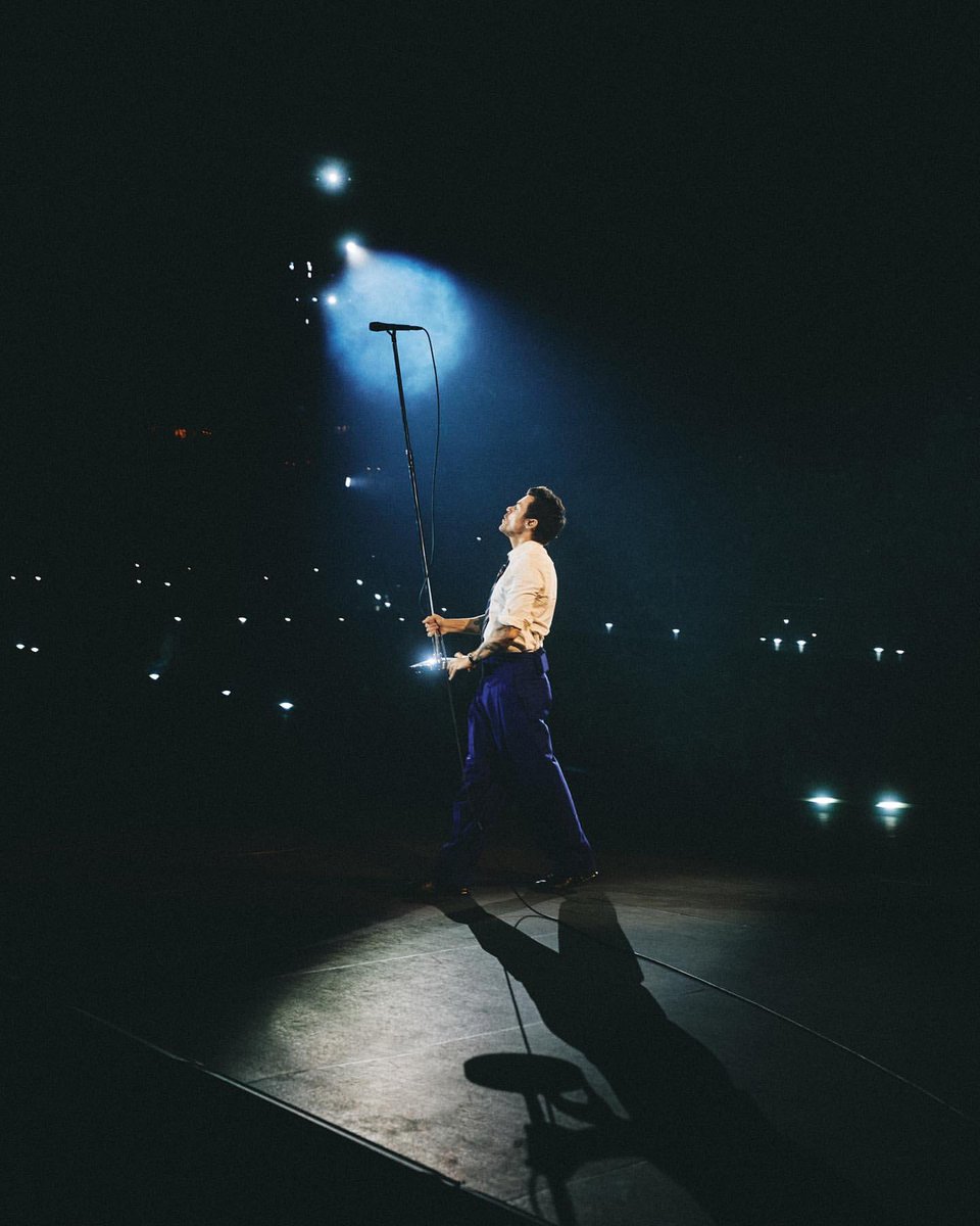 Harry Styles pushes mic stand up into the air for crowd to sing along.
