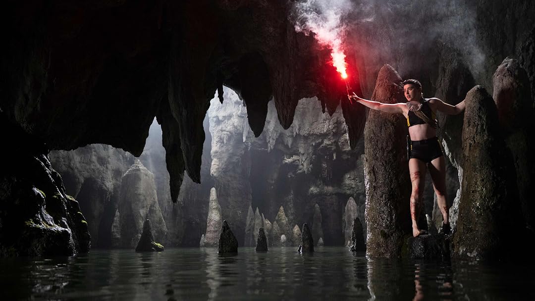 The Devil's Mouth's Sara standing on a stalagmite above the water. She is holding a flare.