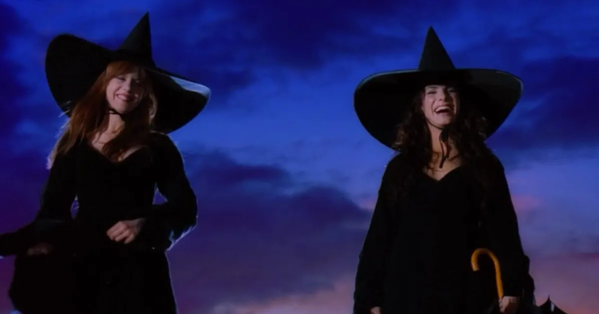 Gillian and Sally in the final scene of Practical Magic. They are smiling while wearing black dresses and witches hats.