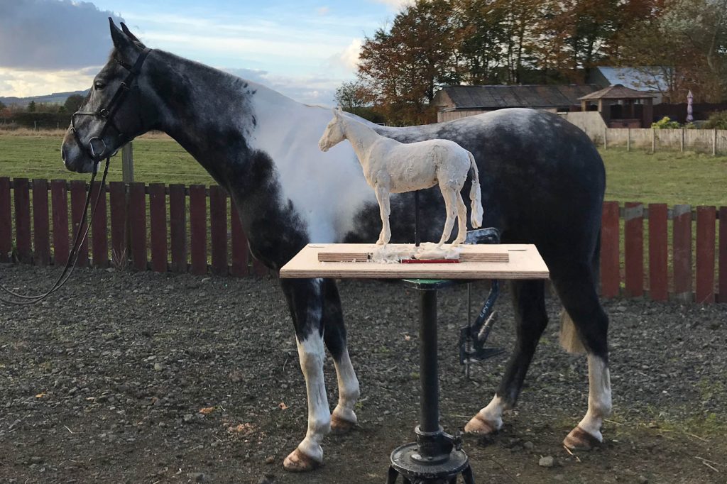 Skewbald horse standing next to a miniature sculpture