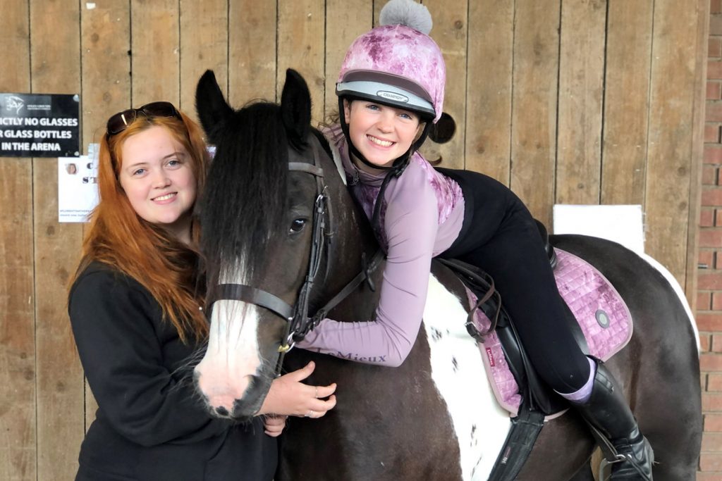 Piebald pony with rider and girl stood by his shoulder