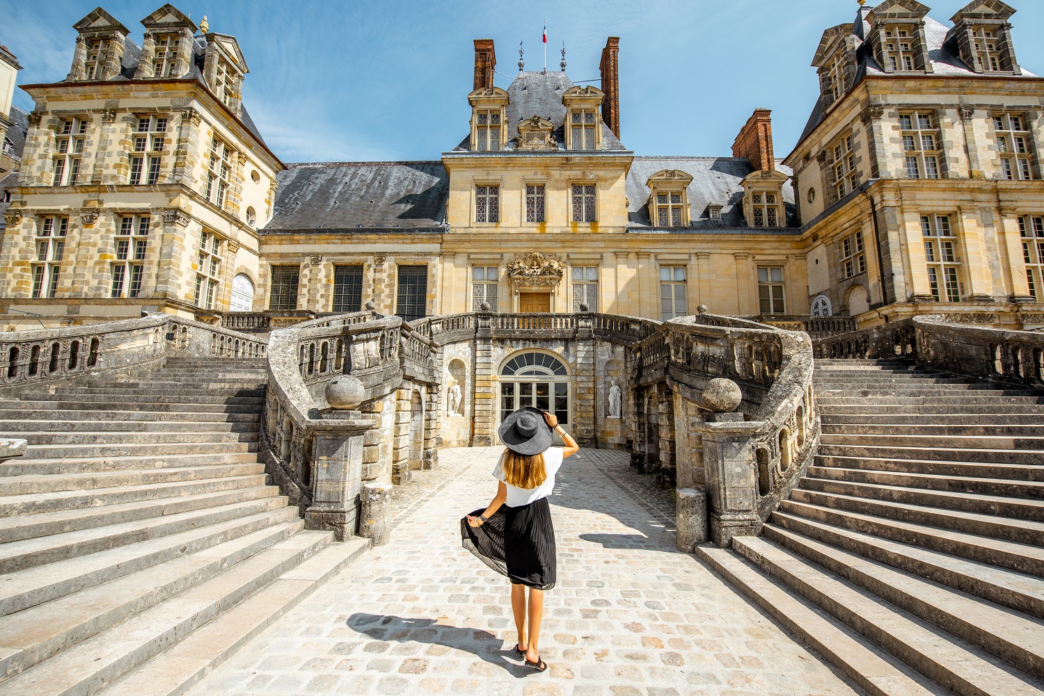 Woman standing back near the beautiful staircase visiting famous Fontainebleau palace in France