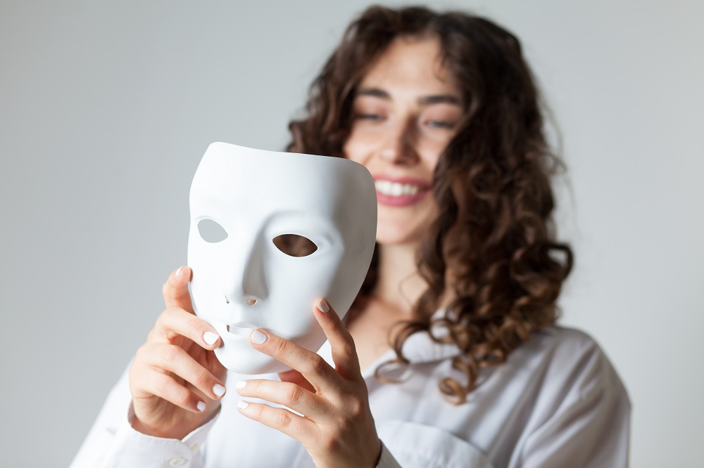 young woman holding a white mask Goddess Unmasked Retreat