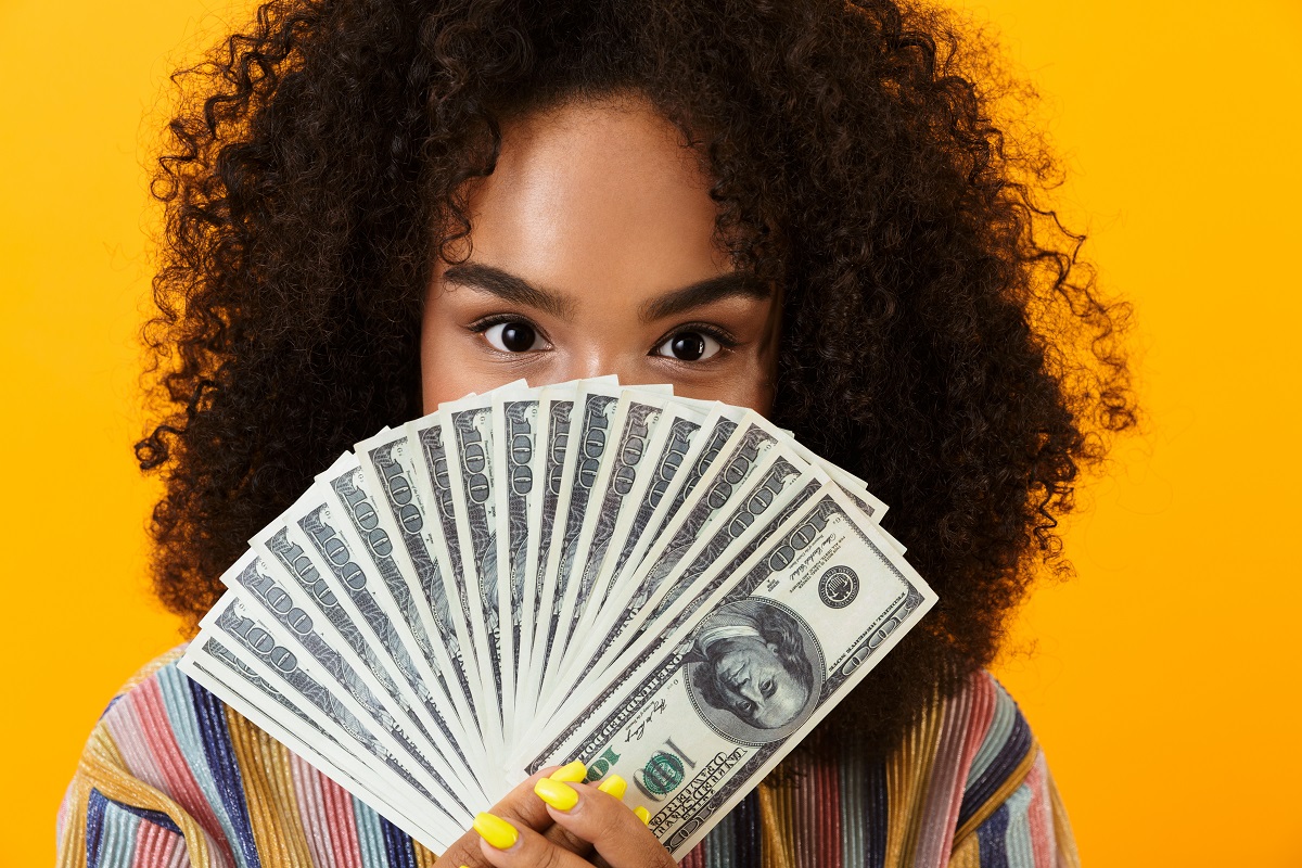 Woman posing isolated over yellow background holding money covering face. Abundance Money Cash