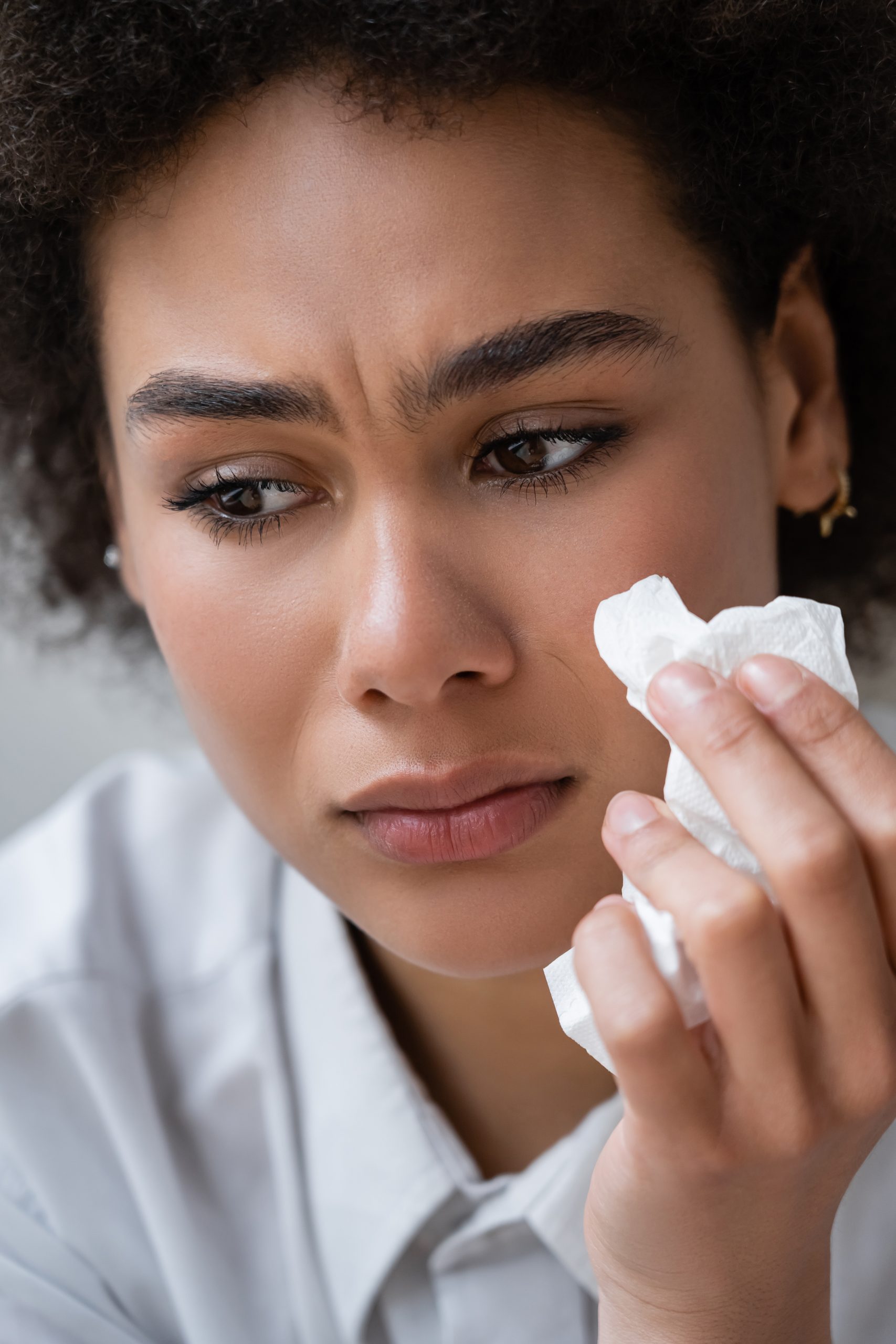 close up of african american woman in white shirt crying and holding napkin.