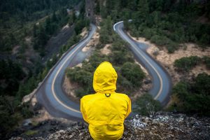 A person in a yellow rain jacket sitting on a cliff overlooking a road