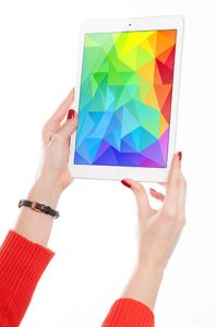 A pair of hands holding up an iPad with a colorful design on it. The person holding the iPad is wearing a watch and has on bright red sleeves.