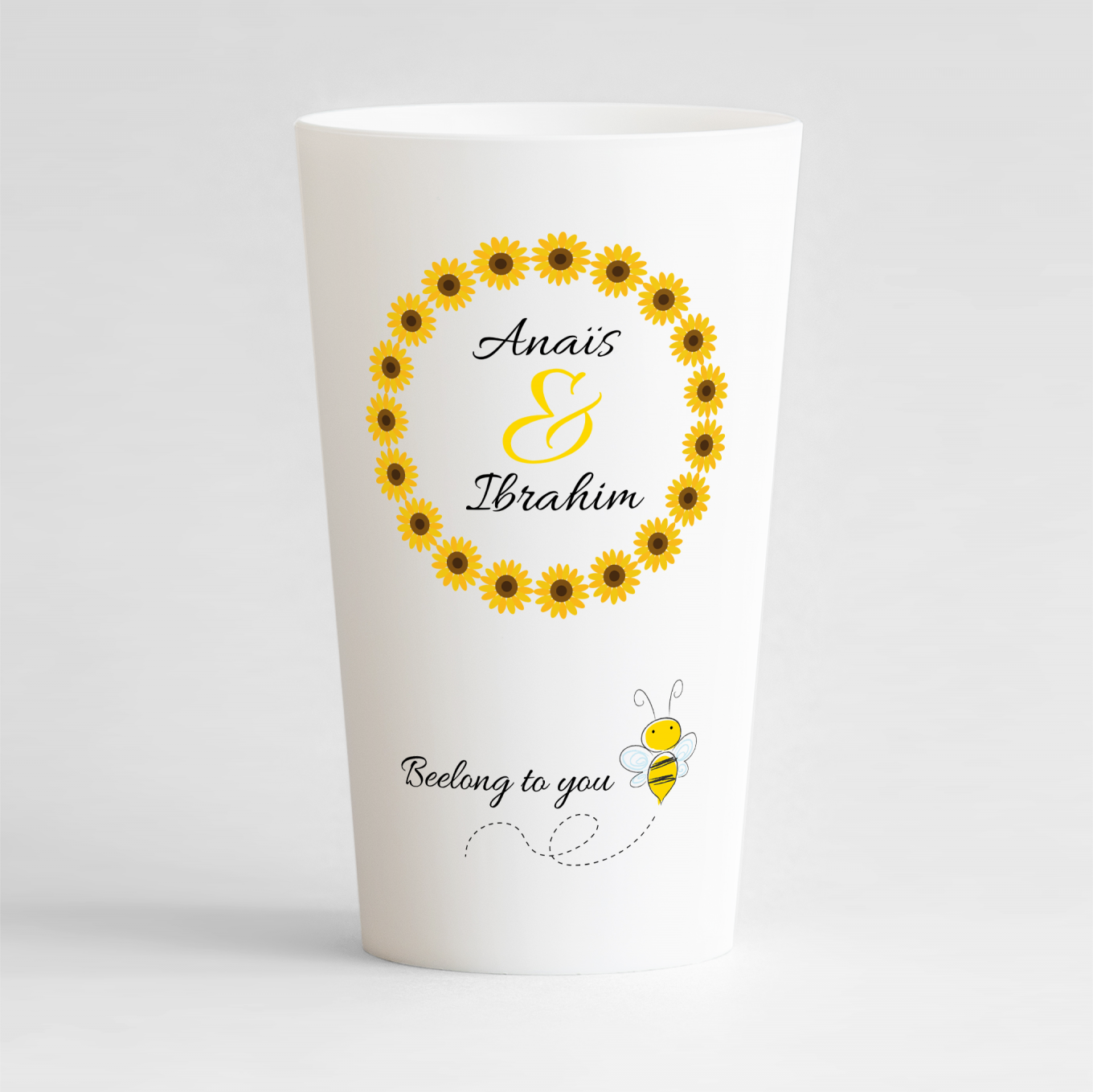 Un ecocup blanc de face avec une couronne de tournesols autour des noms des mariés, et une phrase humour avec une abeille.