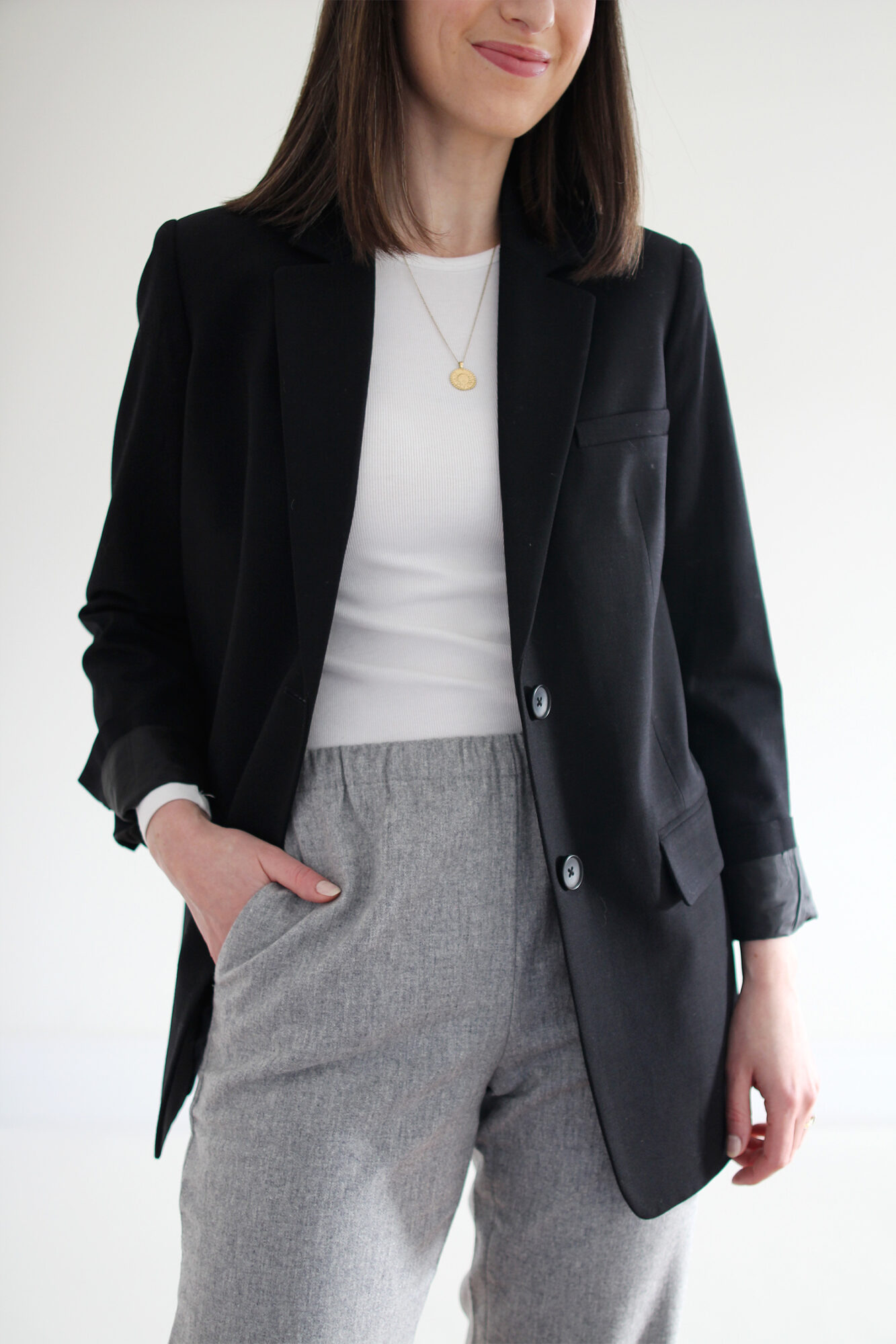 Woman wearing black blazer, white fitted t-shirt, grey joggers, white flats & a gold pendant necklace.