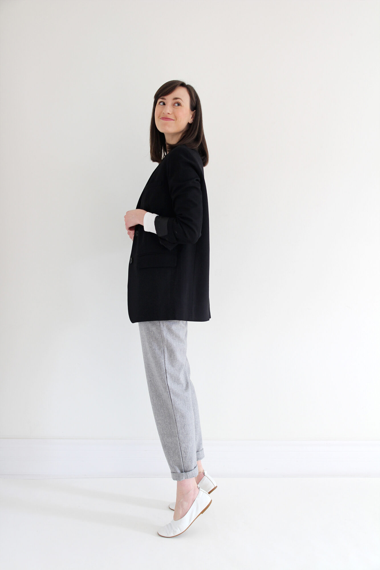 Woman wearing black blazer, white fitted t-shirt, grey joggers, white flats & a gold pendant necklace.