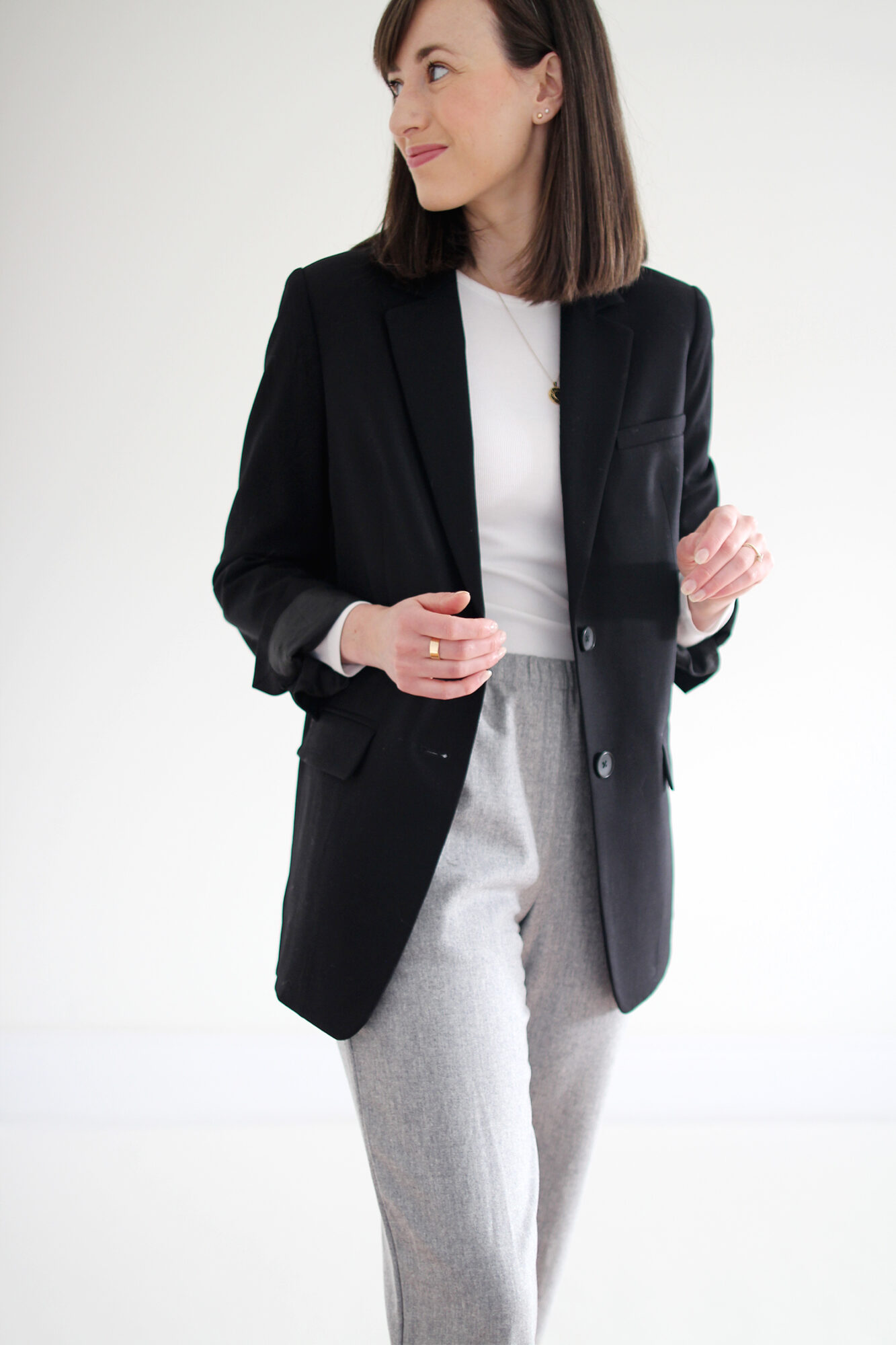 Woman wearing black blazer, white fitted t-shirt, grey joggers, white flats & a gold pendant necklace.