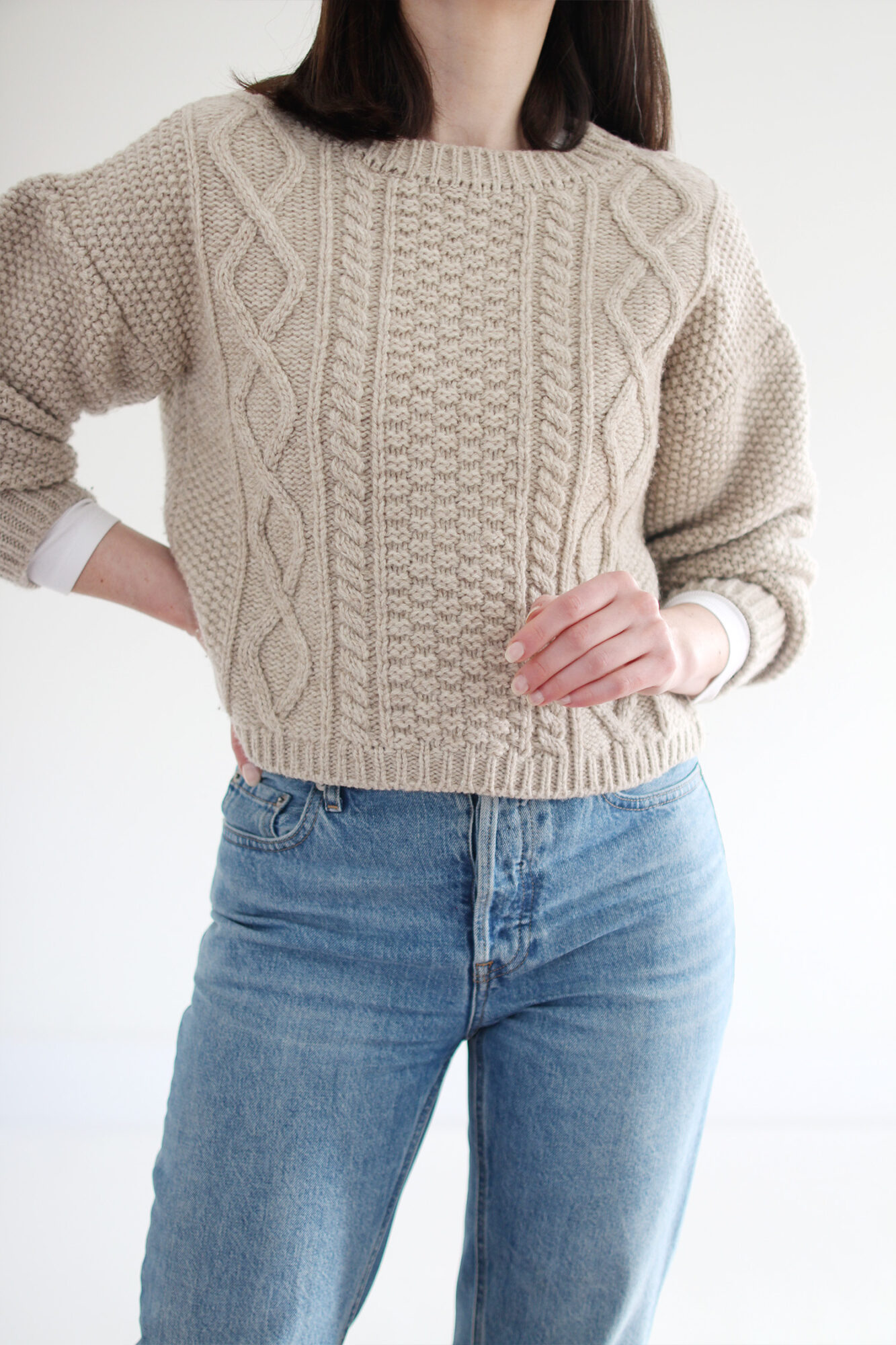 Woman wearing a beige cable knit sweater, vintage blue jeans, a tortoise headband and beige suede lug sole boots.