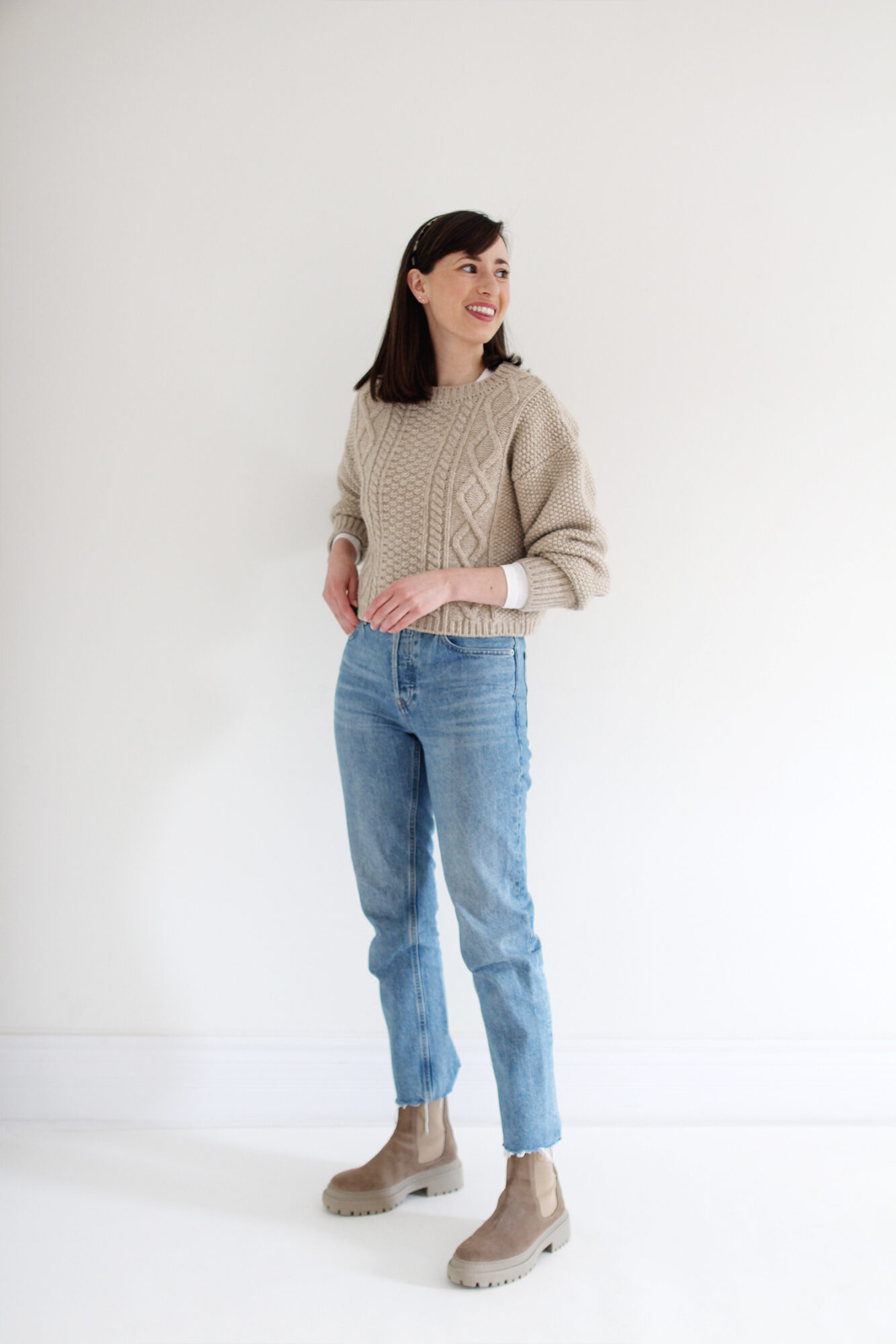 Woman wearing a beige cable knit sweater, vintage blue jeans, a tortoise headband and beige suede lug sole boots.