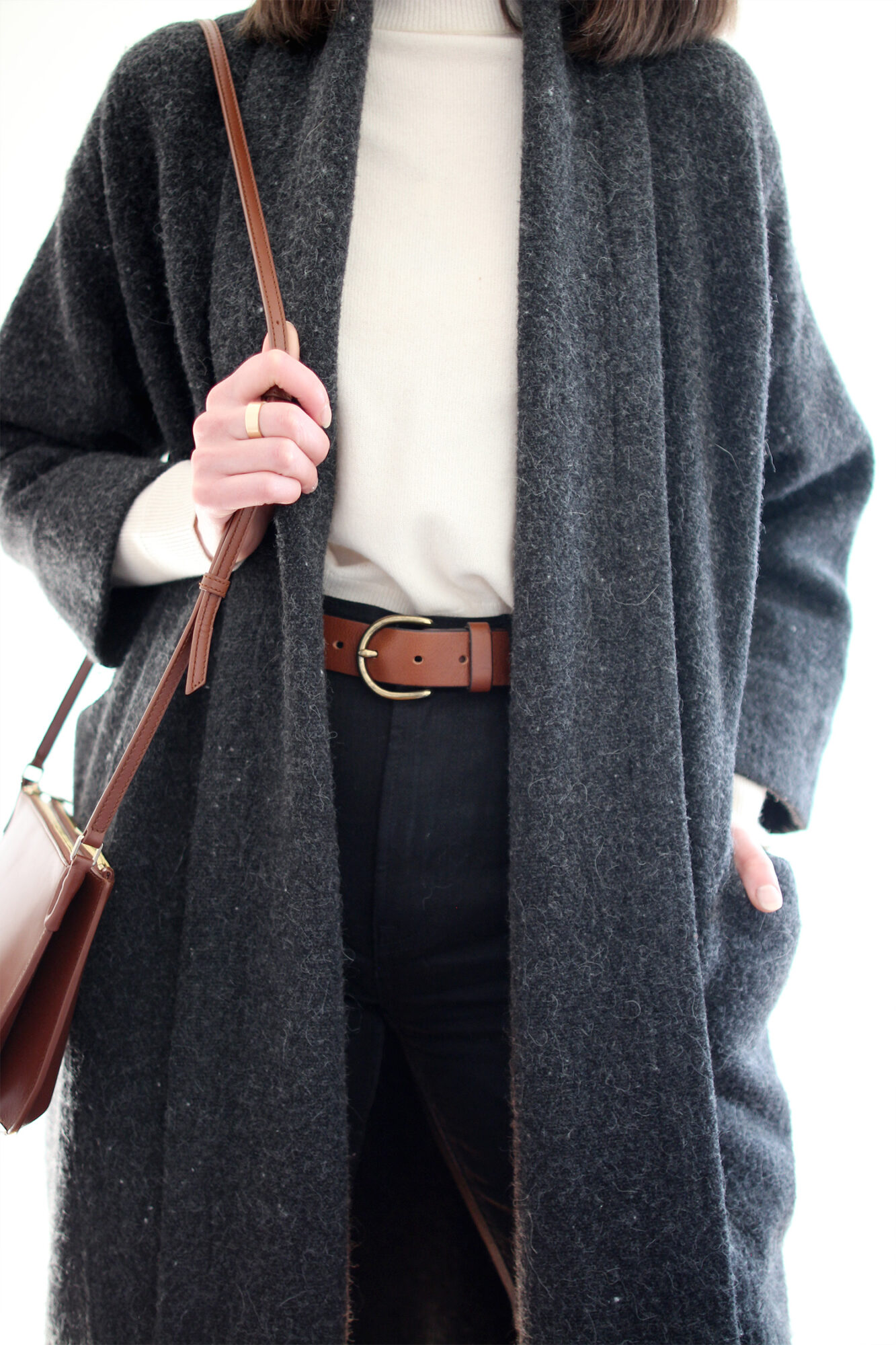 Woman wearing grey wool sweater coat, ivory mockneck sweater, brown leather belt, black jeans, black boots, and brown bag.