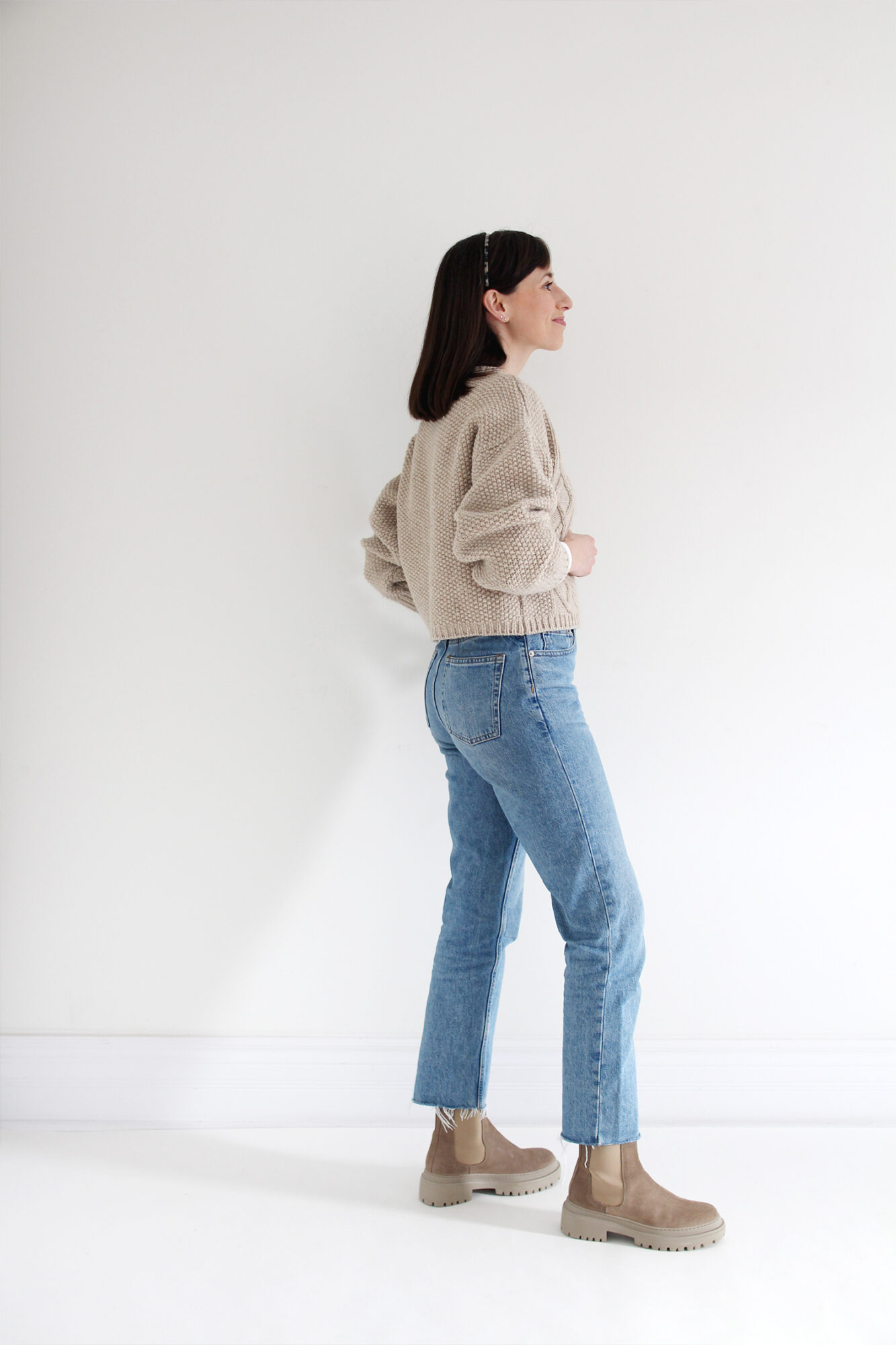 Woman wearing a beige cable knit sweater, vintage blue jeans, a tortoise headband and beige suede lug sole boots.