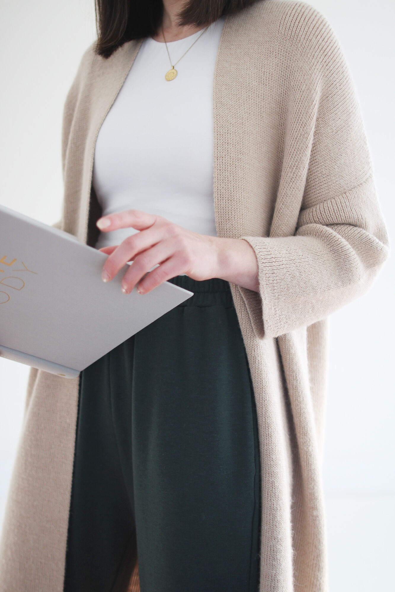 Style Bee wearing a white  fitted top with cropped green lounge pants and a long camel cardigan with shearling slippers.