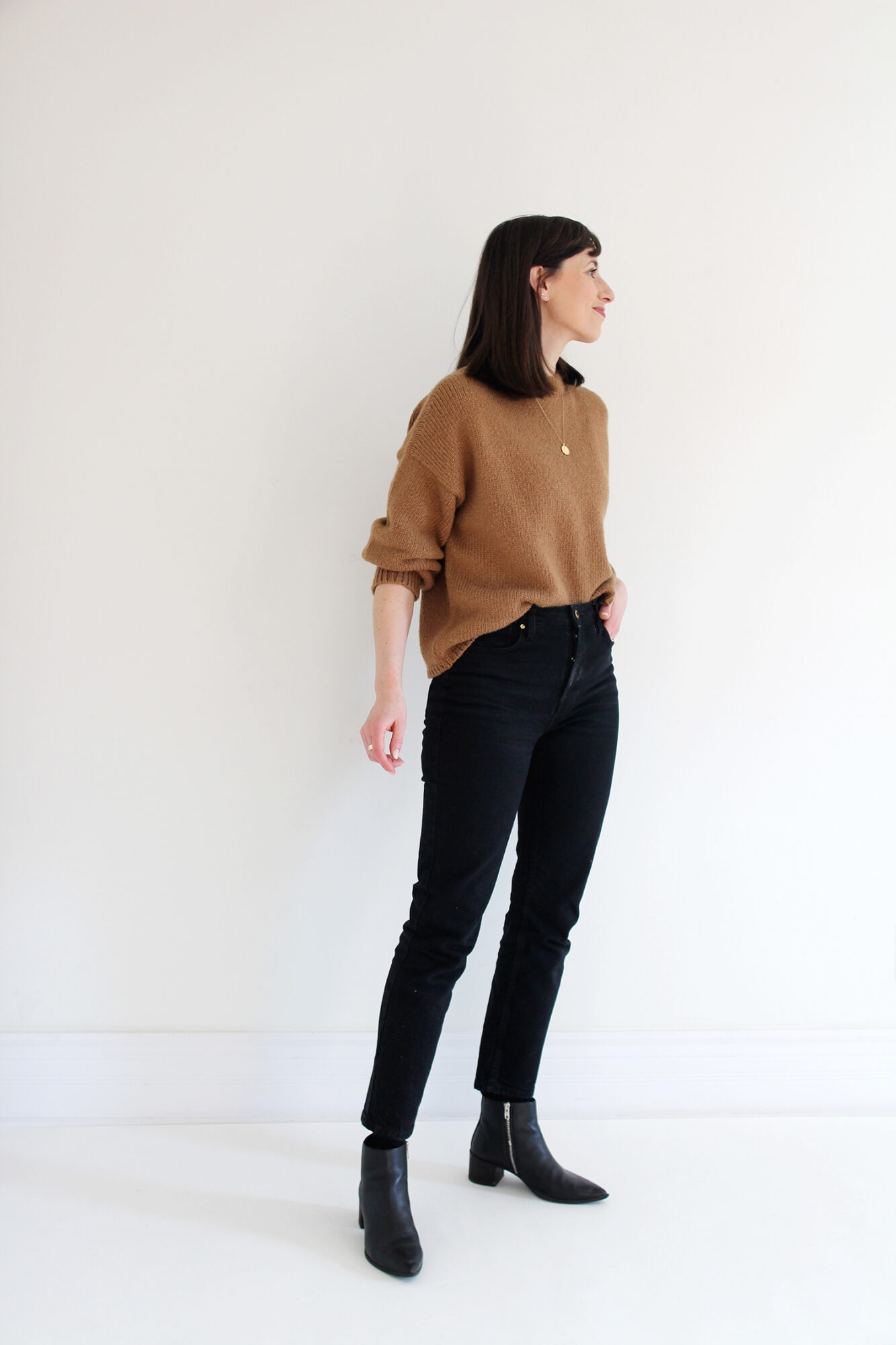 Woman wearing a relaxed alpaca knit sweater in camel, tucked into black jeans with gold jewelry and a tortoise barrette.