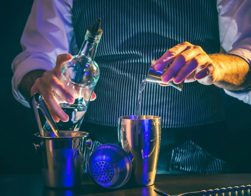 Barman preparando un trago con vodka con la ayuda de una coctelera.