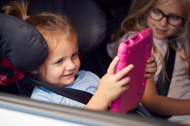 Two Young Girls Watching Digital Tablet In Back Seat On Car Journey