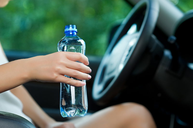 Young woman holding a bottle of water while sitting in the car close up