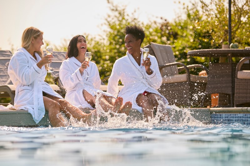 3 mature women in robes with a glass of wine, relaxing by the pool