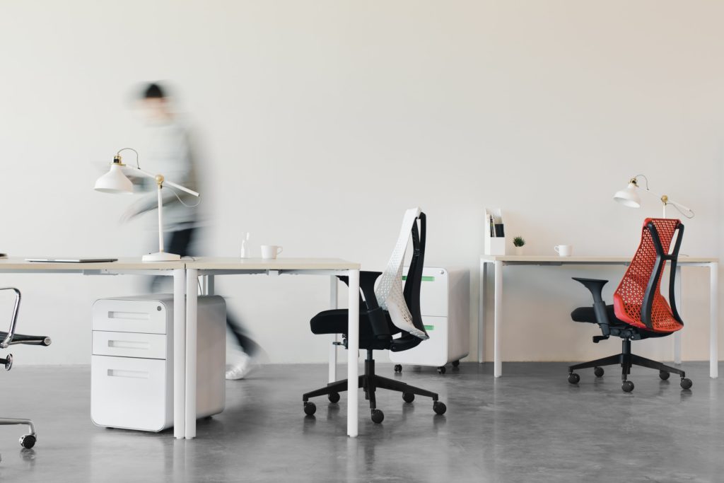A blurred person walking through a modern, minimalist office of chairs and desks.
