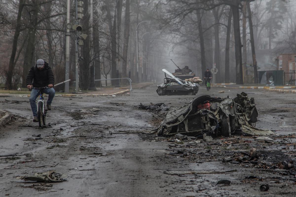 A crumpled passenger car and broken military equipment on the street in Bucha.