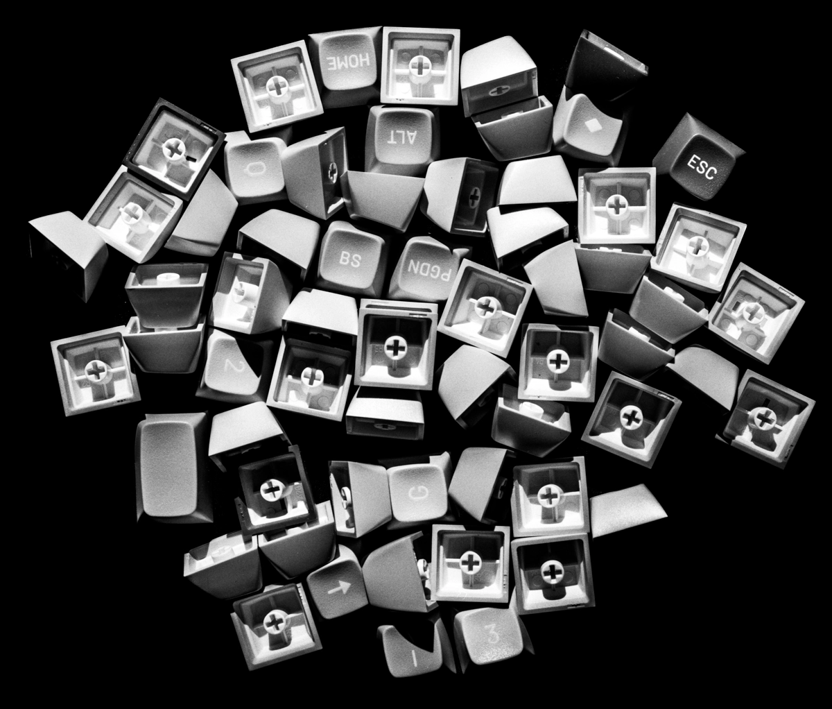 A close-up black-and-white photograph of a dramatically-lit pile of loose keyboard keys