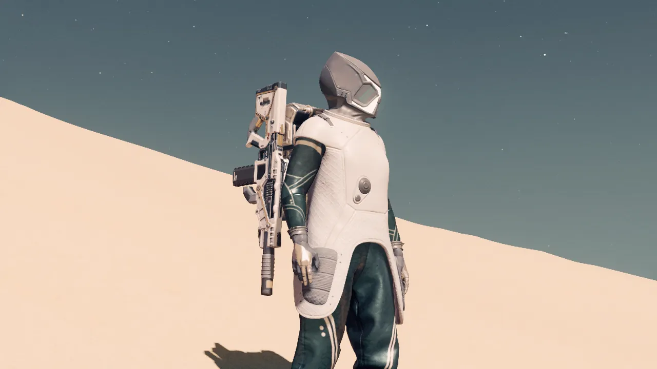 A figure in an alien-like space suit stands in a desert. The slope of a dune cuts the frame in contrast with the sky
