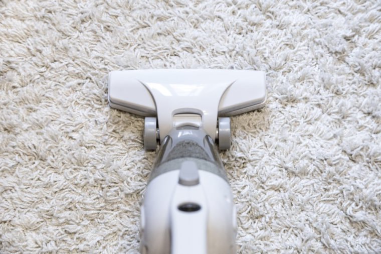 Vacuuming rough white carpet in living room with vacuum cleaner