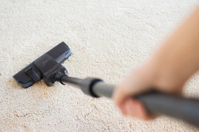 people, housework and housekeeping concept - close up of hand with vacuum cleaner cleaning carpet at home