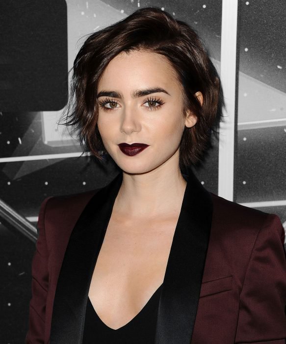 Lilly Collins usando un labial negro con un traje color vino 