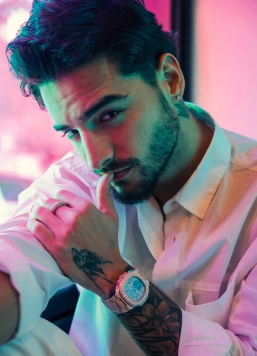 Cantante Maluma posando para una fotografía mientras usa una camisa blanca, pantalón negro y reloj se oro