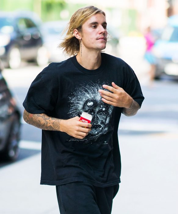 Chico de cabello largo y rubio caminando en la calle con playera holgada negra