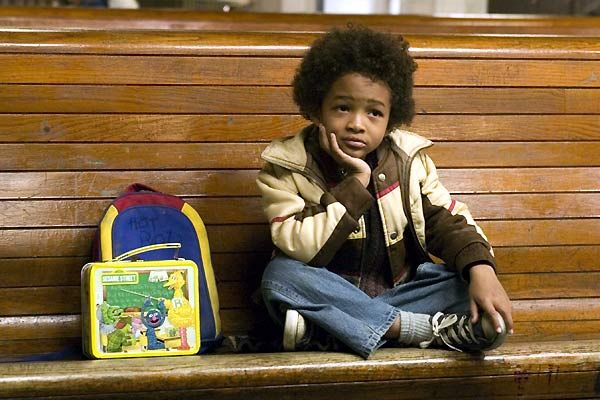 Niño de cabello chino sentado en una banca de madera con su mochila