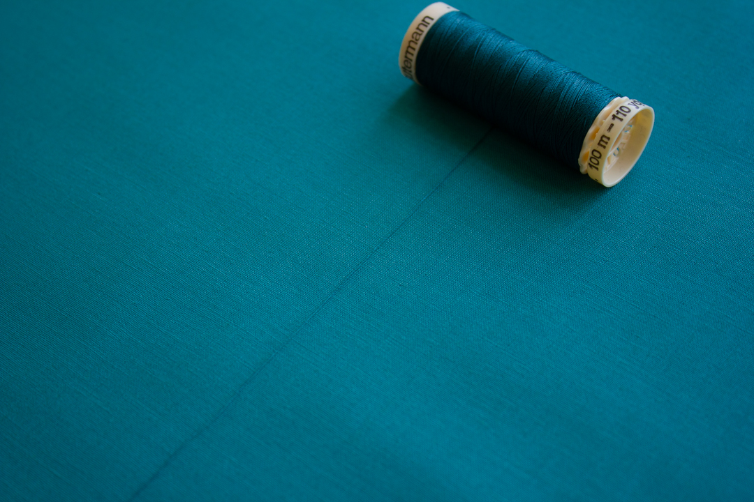 A spool of blue thread is pictured on a background of blue fabric. The thread is unwound a bit, to show that the thread color matches the fabric color. 