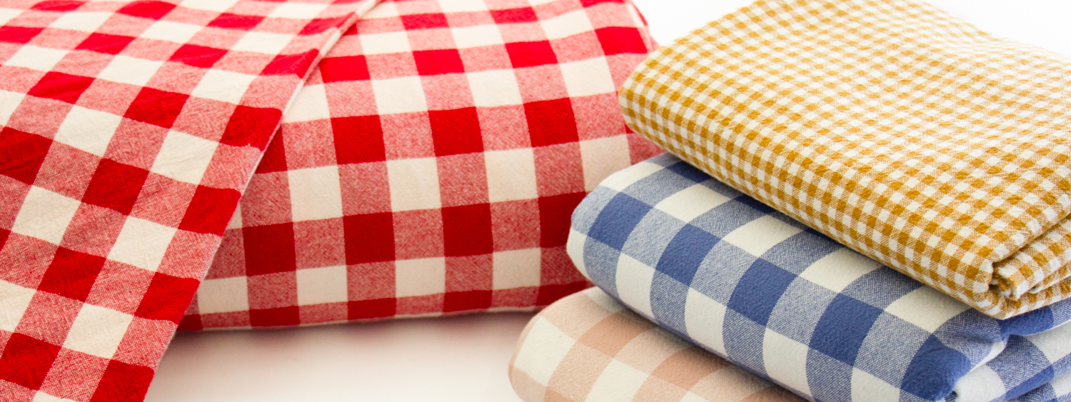 Checkered fabric rolls in red, yellow, and blue hues stacked together, showcasing a variety of patterns suitable for sewing and crafting projects.