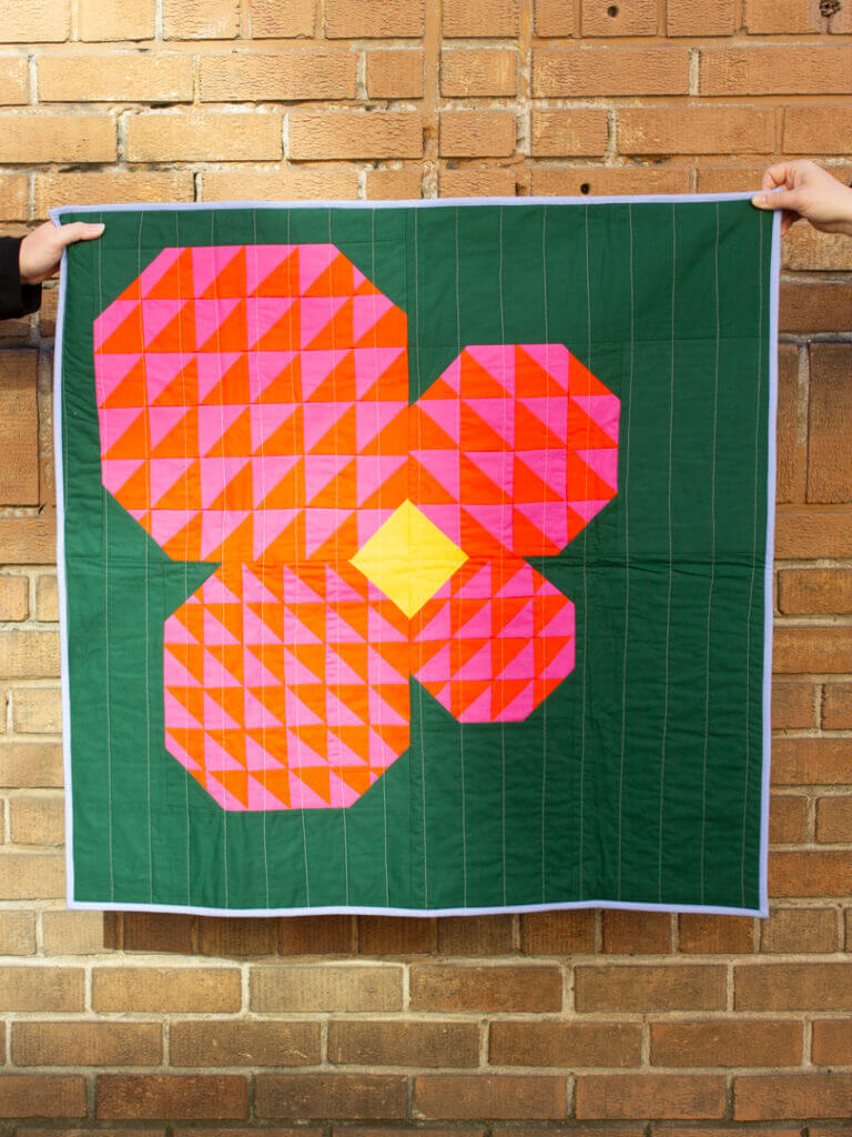 Colorful quilt featuring a geometric flower design on a green background.