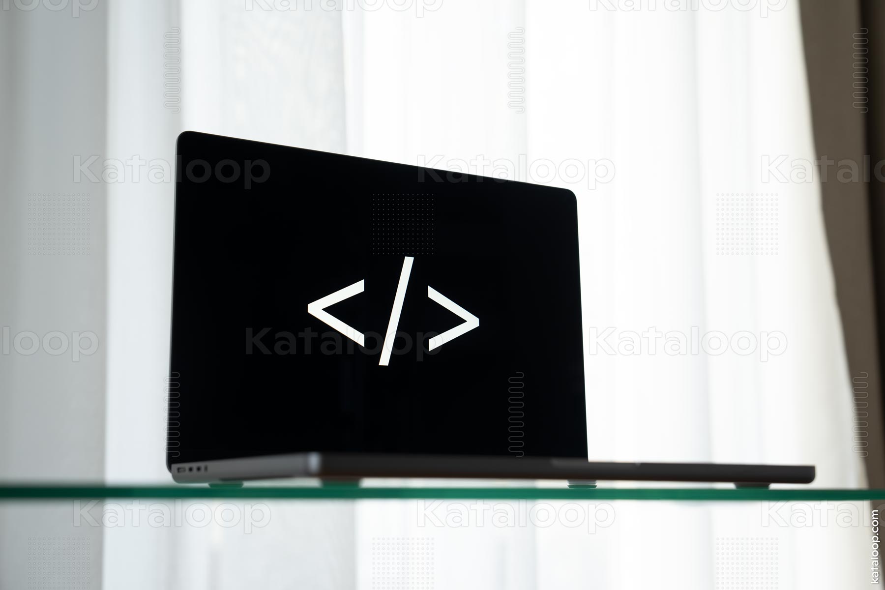This image features a laptop on a glass desk displaying a symbol commonly associated with coding, specifically angle brackets used in markup languages. The laptop is closed and the symbol is illuminated on the screen, creating a striking contrast with the dark background.