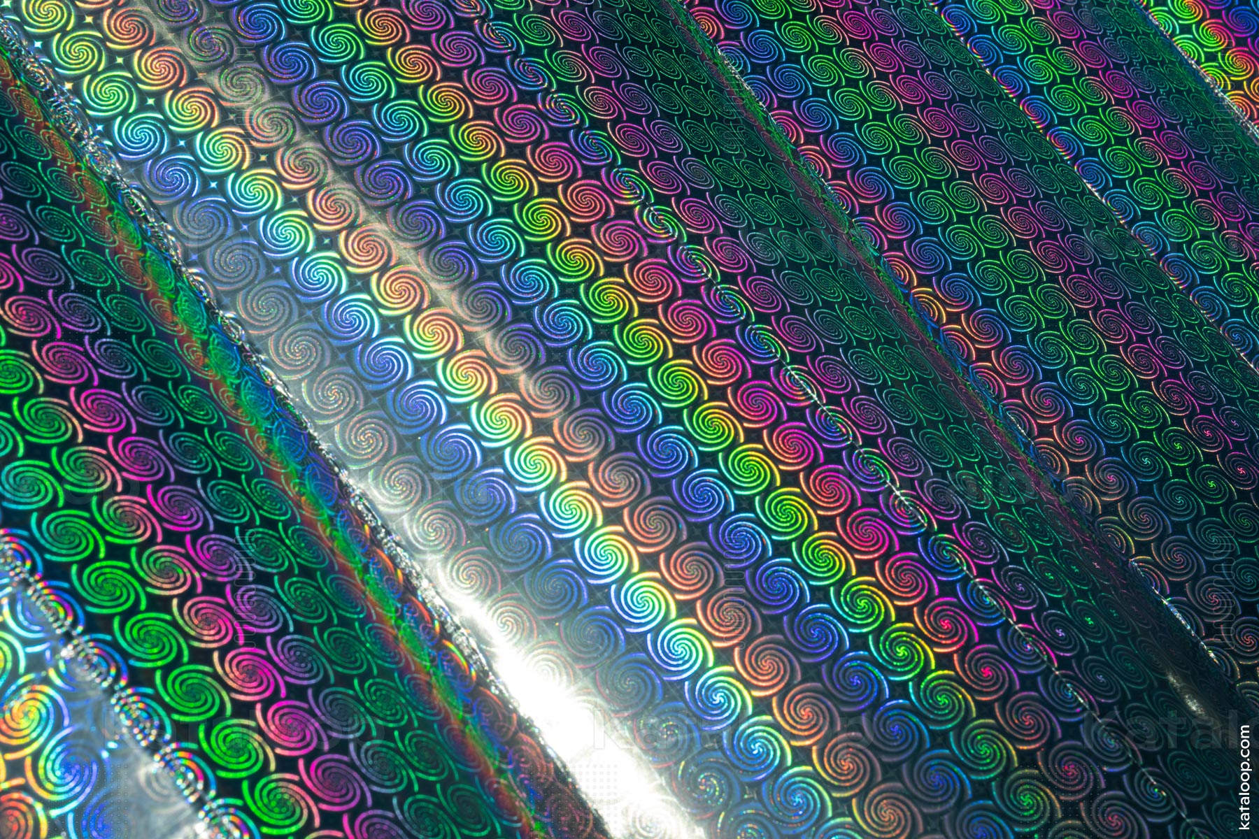 This image captures the vibrant and iridescent spiral patterns found on a holographic surface. The play of light creates a spectrum of colors that shift and change depending on the viewing angle. The detailed texture adds depth and dimension to the visual experience.