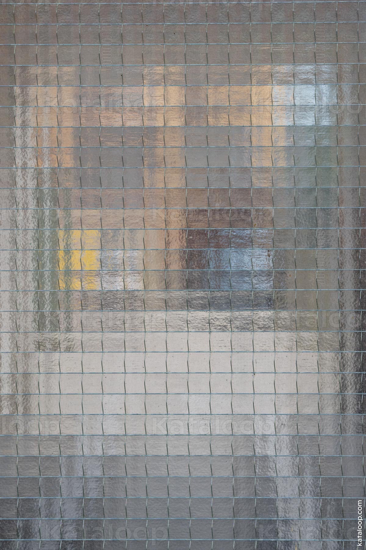This image captures an abstract reflection on a grid of a glass surface. The reflection is distorted, creating an intriguing mosaic effect. The varying shades and tones suggest a reflection of a cityscape or buildings.