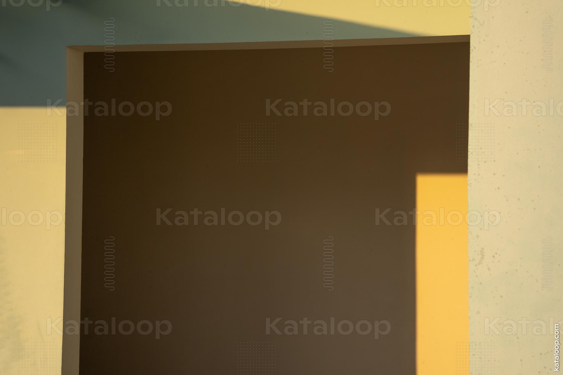 This image features an interplay of geometric shapes created by walls and shadows. The soft light casts a warm yellow hue against the textured surfaces, creating a visually striking contrast. The composition emphasizes the simplicity and elegance of architectural forms. The shadows add depth and intrigue to the overall aesthetic.