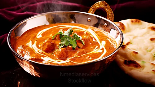 Creamy chicken tikka masala in a copper bowl, garnished with cilantro and cream swirl, with naan bread beside — 8K royalty-free food & beverage stock photo