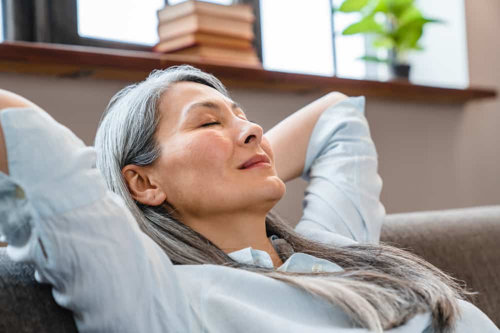 A senior woman with her arms behind her head relaxing on a couch