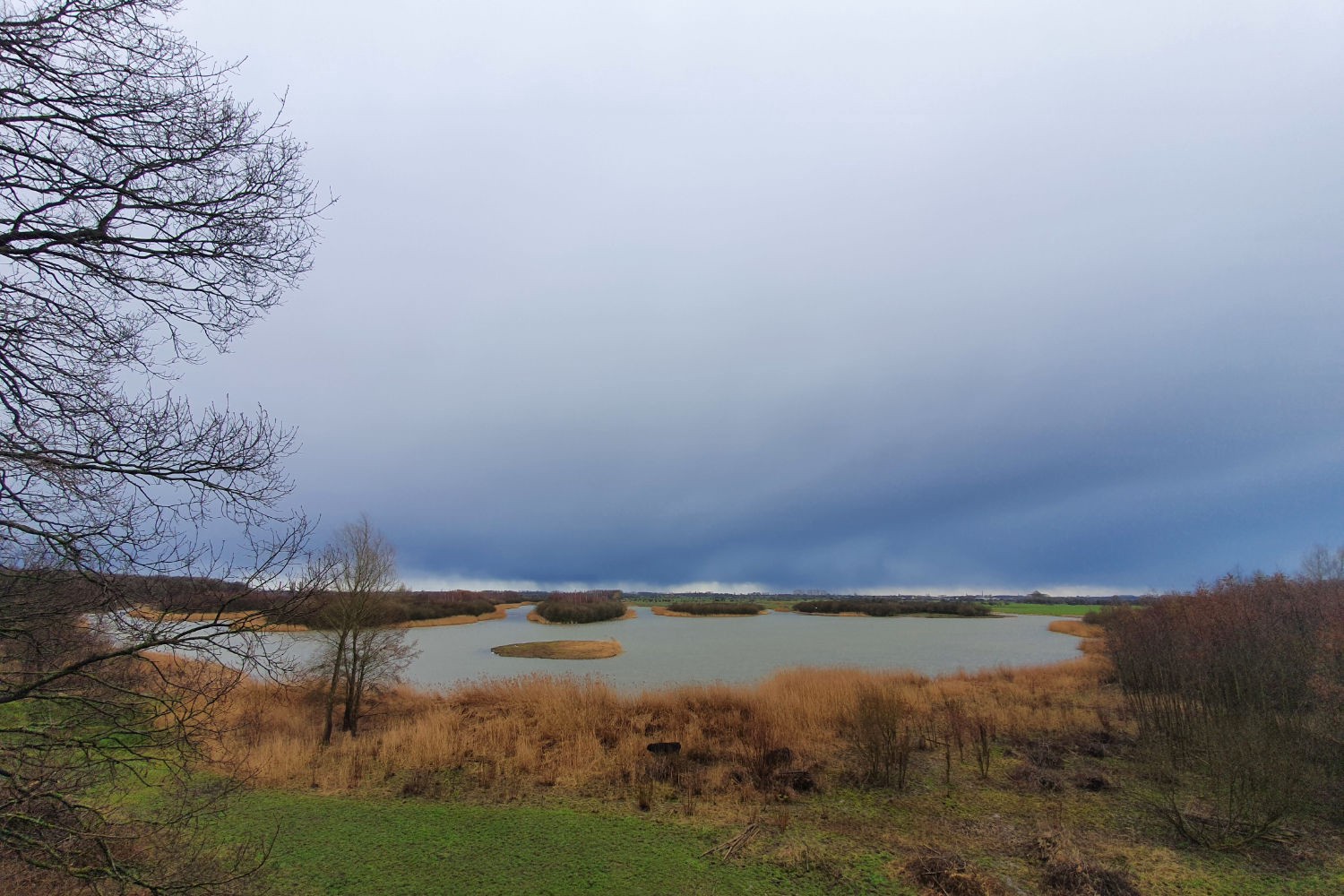 View of the Dutch countryside from a look-out tower with a lake and meadows in the background. A storm is coming.