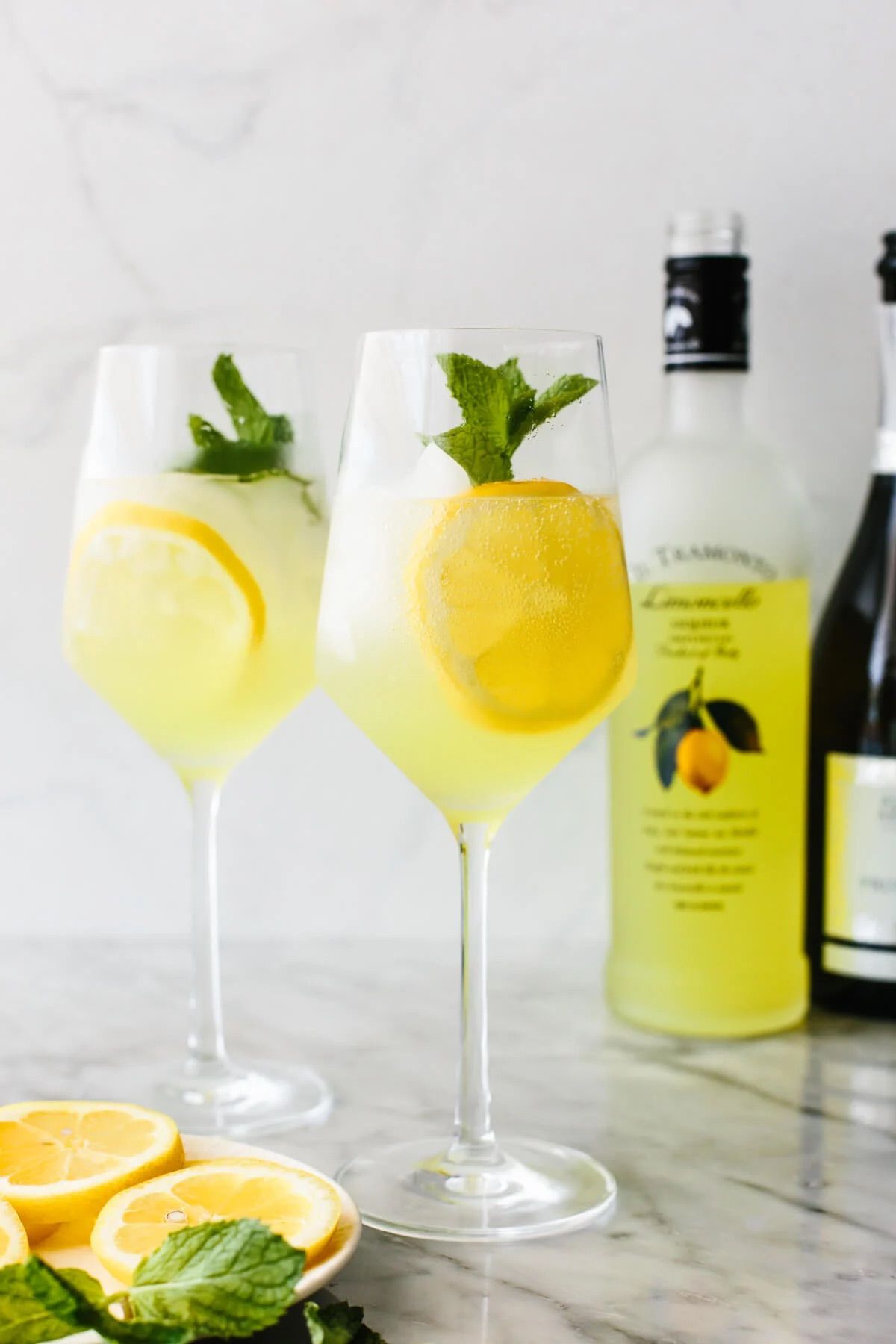 2 glasses of a lemon drink with mint leaves and a bottle of liquor
