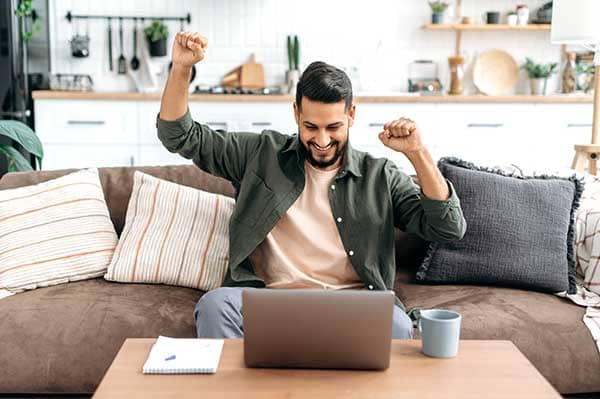 homme heureux devant son ordinateur qui a les bras levés