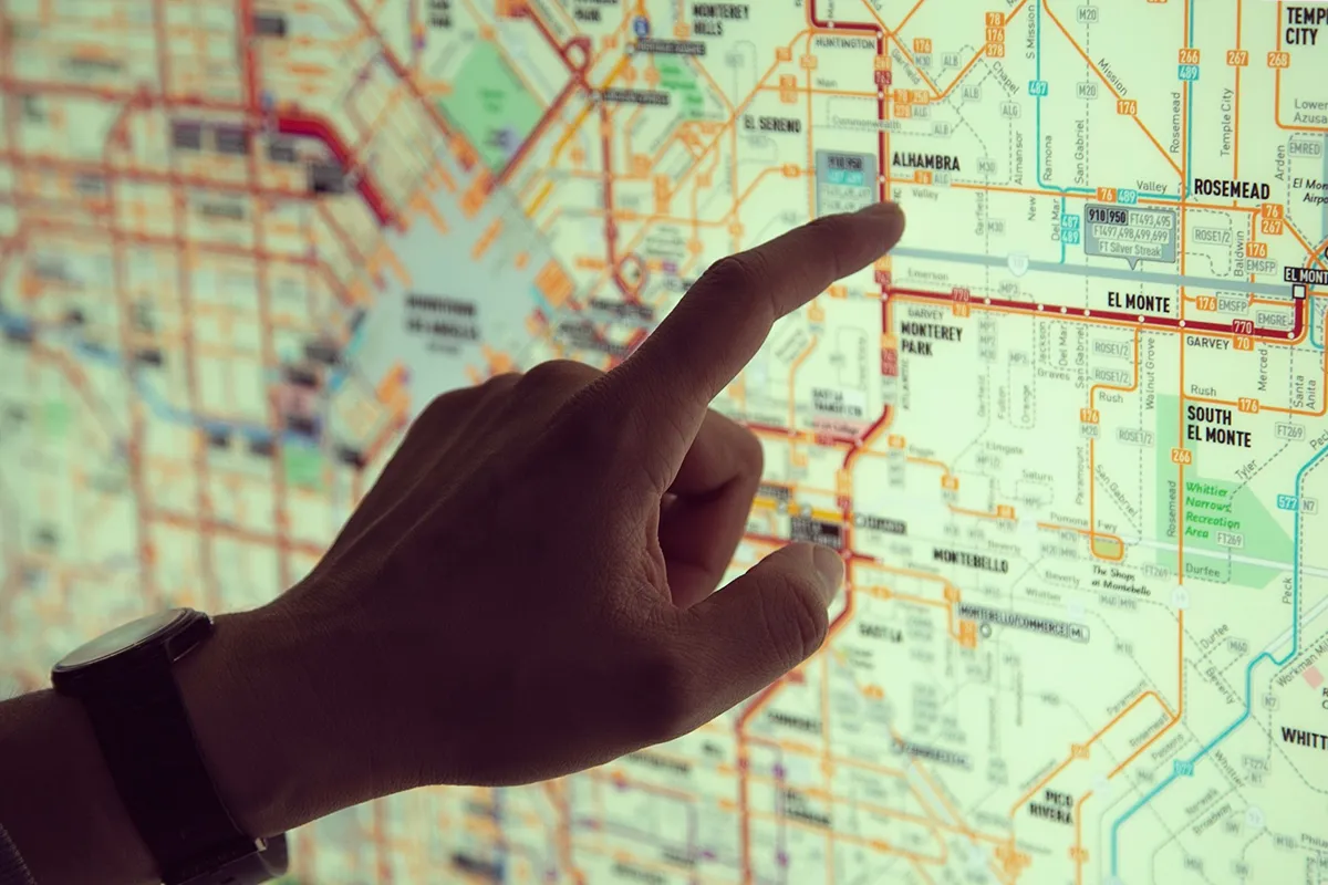 ロサンゼルス地域の交通マップを指さしている人の手。地図上にはEl Monte、Rosemead、Alhambra地区などが表示され、カラフルな路線が描かれている。