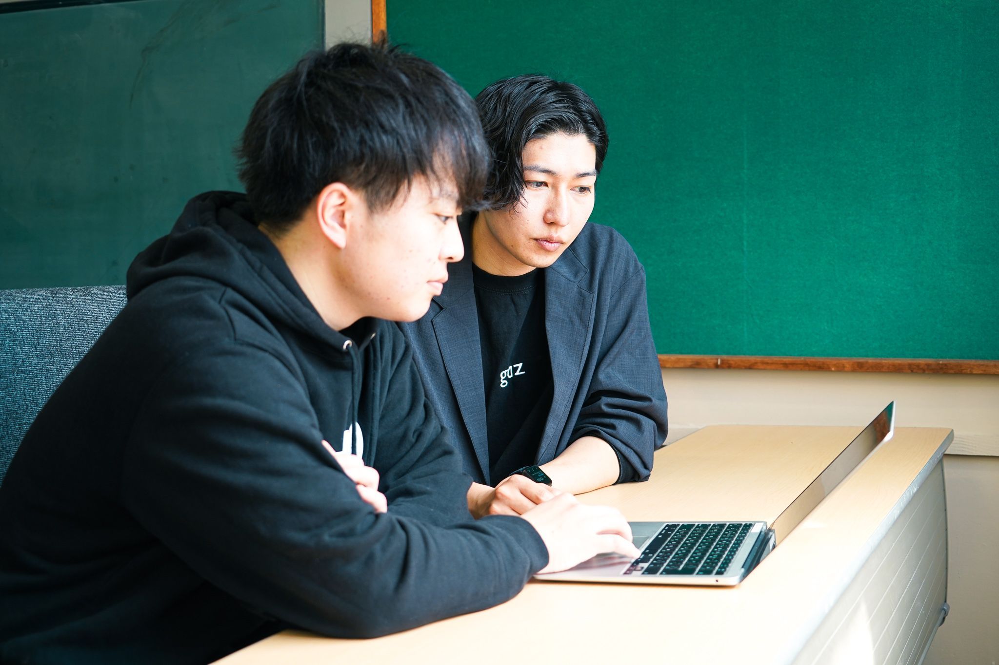 ノートパソコンを操作する崎山さんと、左から覗き込む吉岡さんを、崎山さん側から見た風景